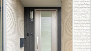 A modern building entrance with a glass door, a mailbox, and a small outdoor area with steps. - THE SHIMMER FURANO (Furano)
