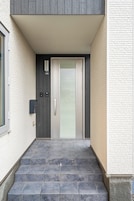 Una entrada moderna de edificio con puerta de vidrio, buzón y un pequeño espacio exterior con escalones.