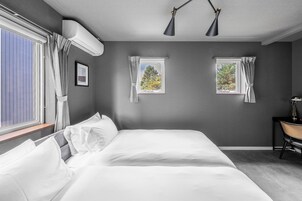 Un dormitorio con una cama grande, dos ventanas con cortinas, un escritorio con una silla y un equipo de aire acondicionado.