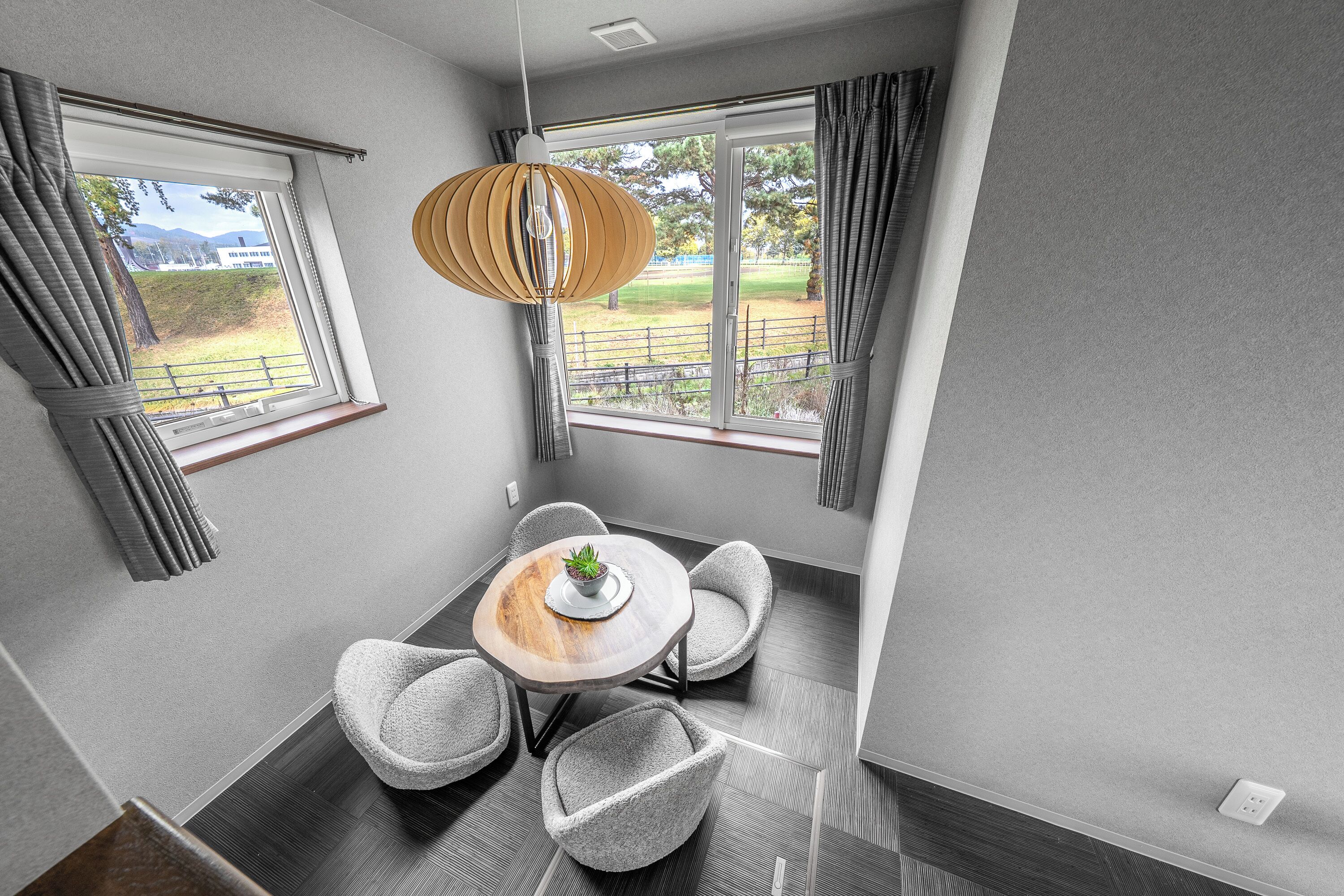 A modern room with a dining table, four chairs, a hanging light fixture, and large windows with curtains.