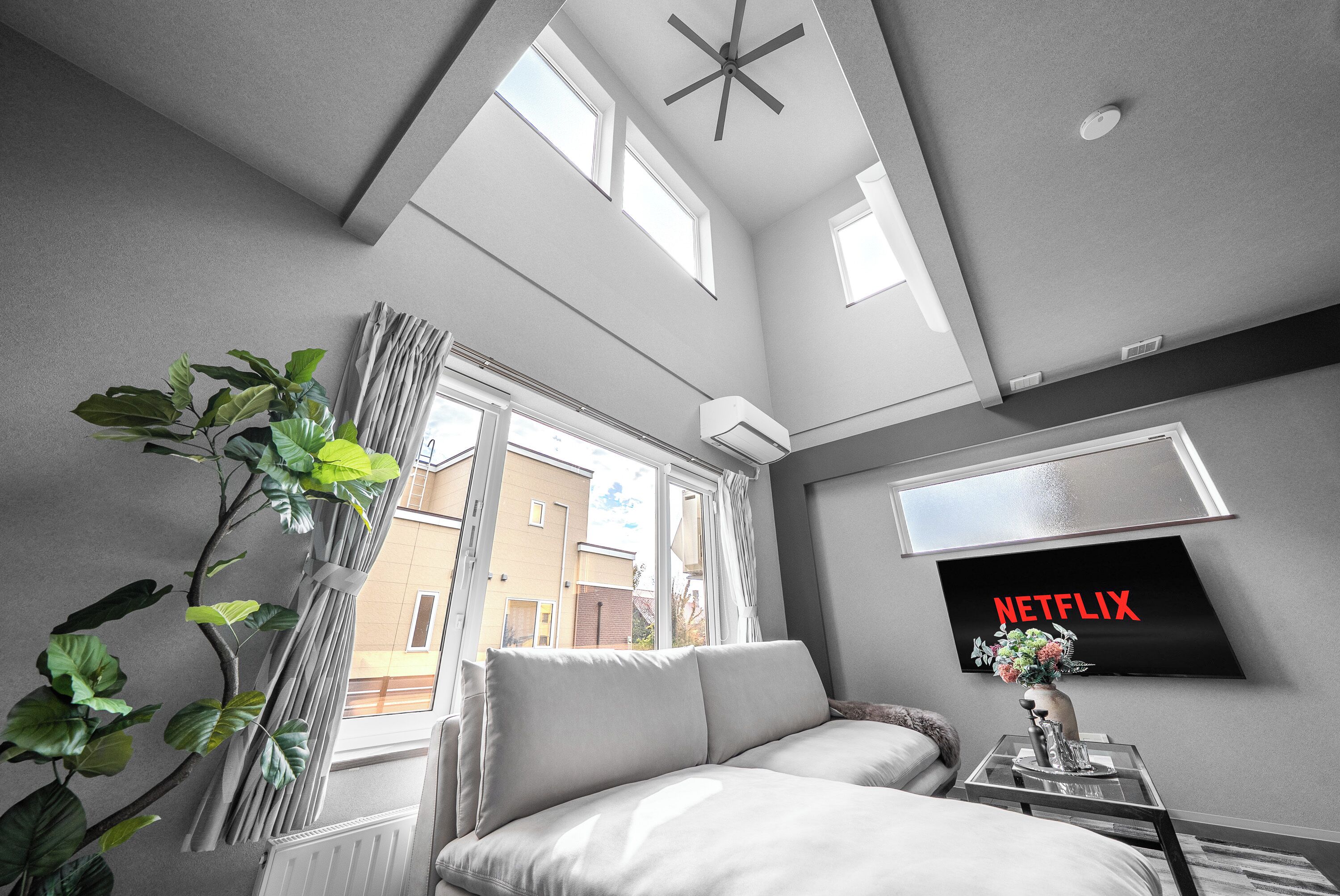 A modern bedroom with a large bed, a TV mounted on the wall, and a view of the outside through a window.