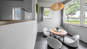 A modern room with a wooden dining table, two upholstered chairs, a hanging light fixture, a window with curtains, and a staircase. - THE SHIMMER FURANO (Furano)