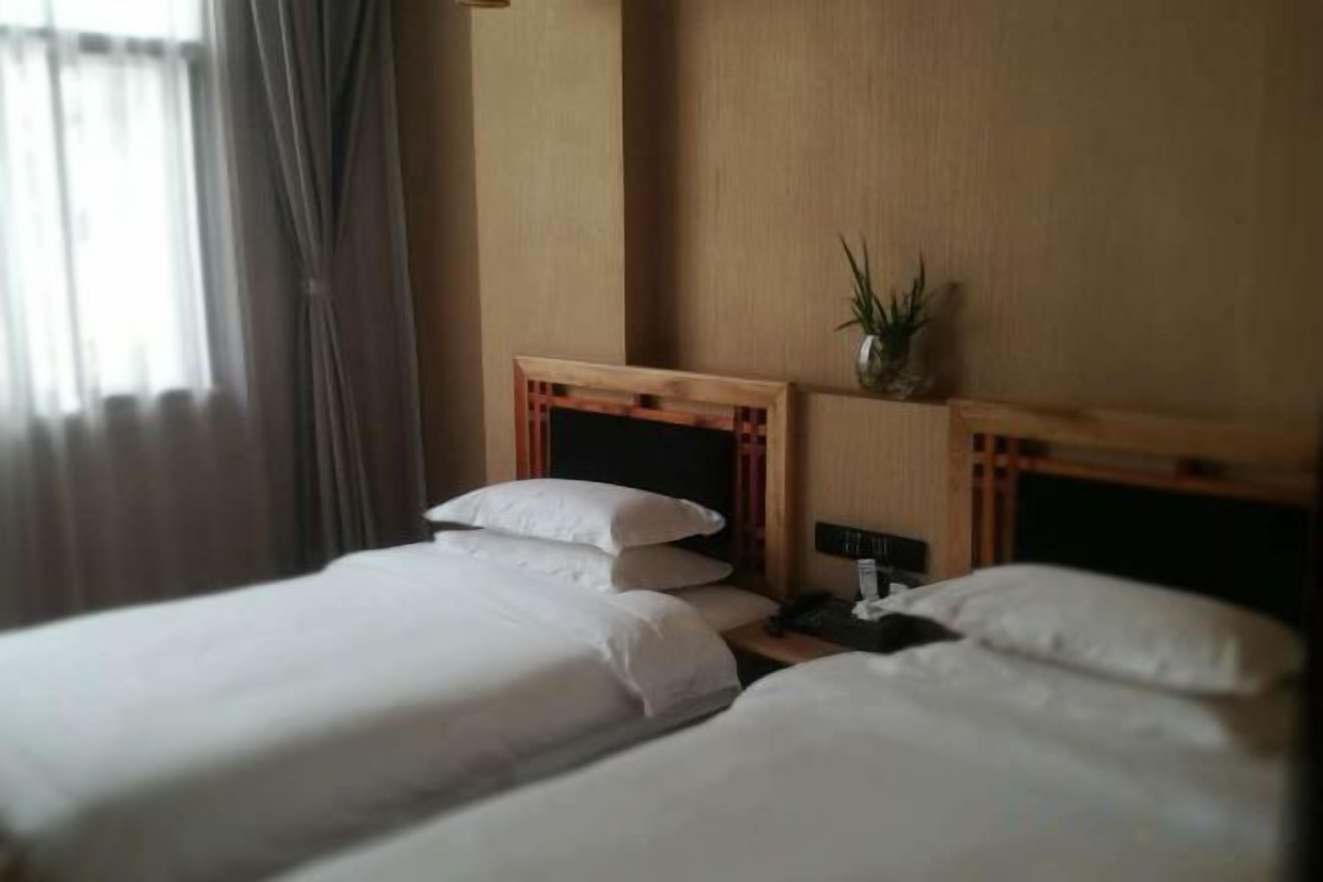Una habitación de hotel con dos camas individuales, una mesita de noche, una lámpara y una planta en maceta.