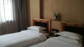 Una habitación de hotel con dos camas individuales, una mesita de noche, una lámpara y una planta en maceta.
