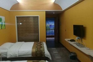 Habitación de hotel con cama, escritorio con computadora, televisor y puerta que da a un balcón.