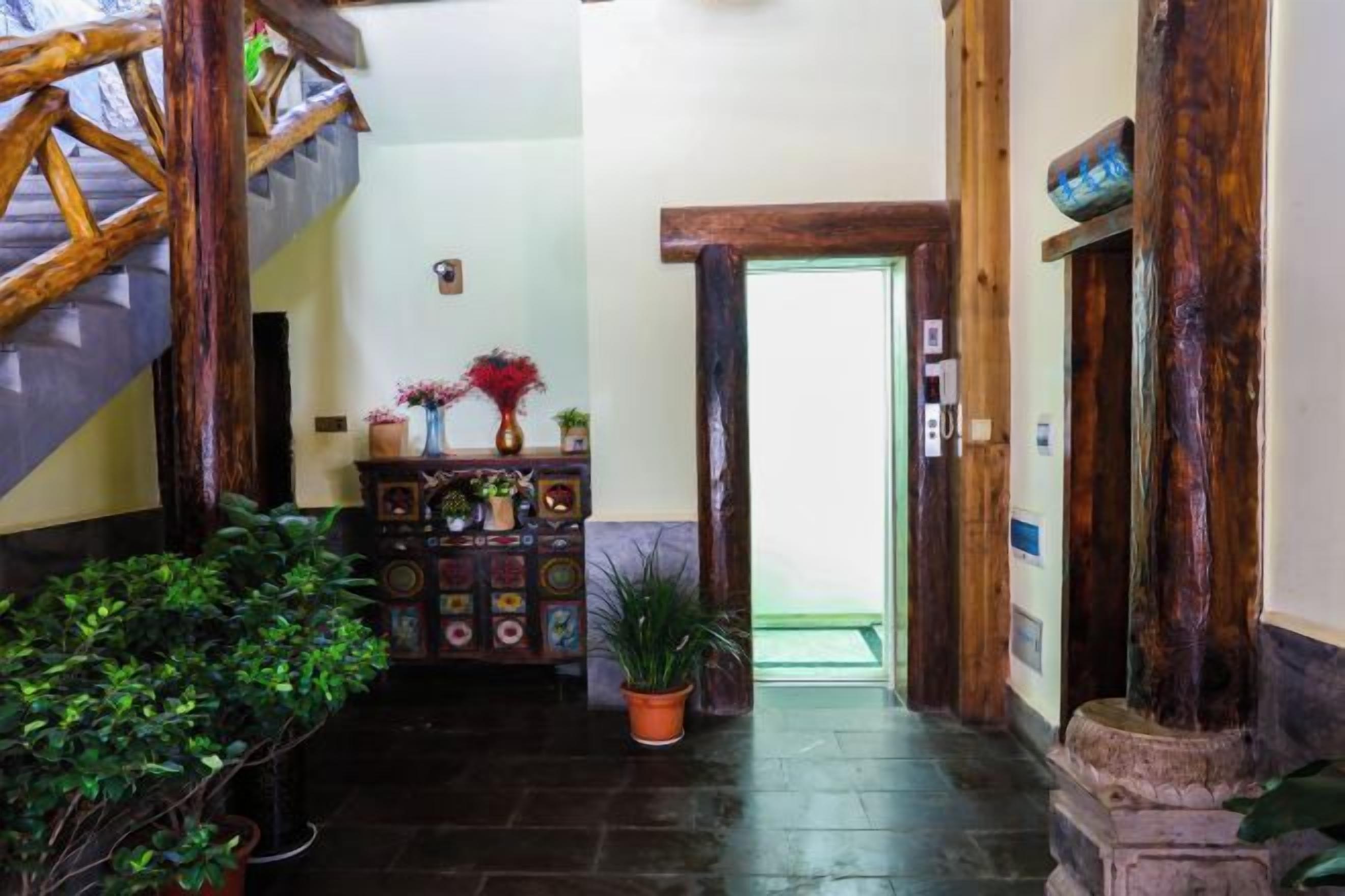 Een hal met een houten trap, een decor kast met planten, en een deur naar een andere kamer.