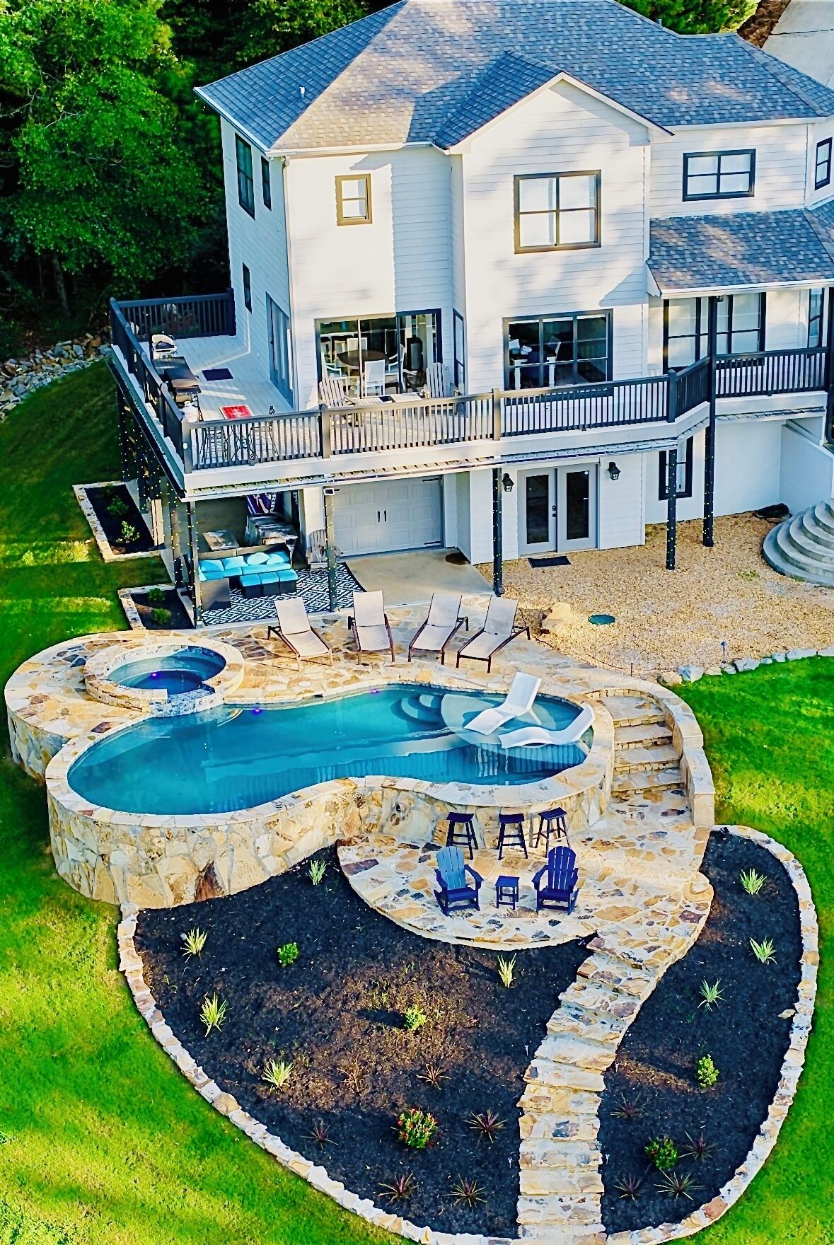 Une maison à deux étages dotée d’un grand jardin à l’arrière, comprenant une piscine, un espace salon extérieur et un chemin en pierre.