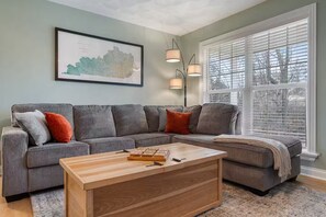A living room with a gray sectional sofa, a wooden coffee table, and a framed map on the wall. - Spacious, Pristine Home w/ Firepit, Bourbon Lounge (Bardstown)