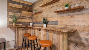 Een rustieke bar met houten lambrisering, twee krukken en decoratieve planten.