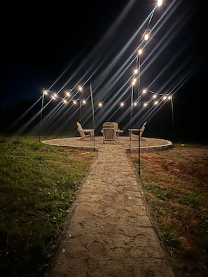 Ein Sitzbereich im Freien mit Stühlen und Tischen unter Lichterketten bei Nacht.
