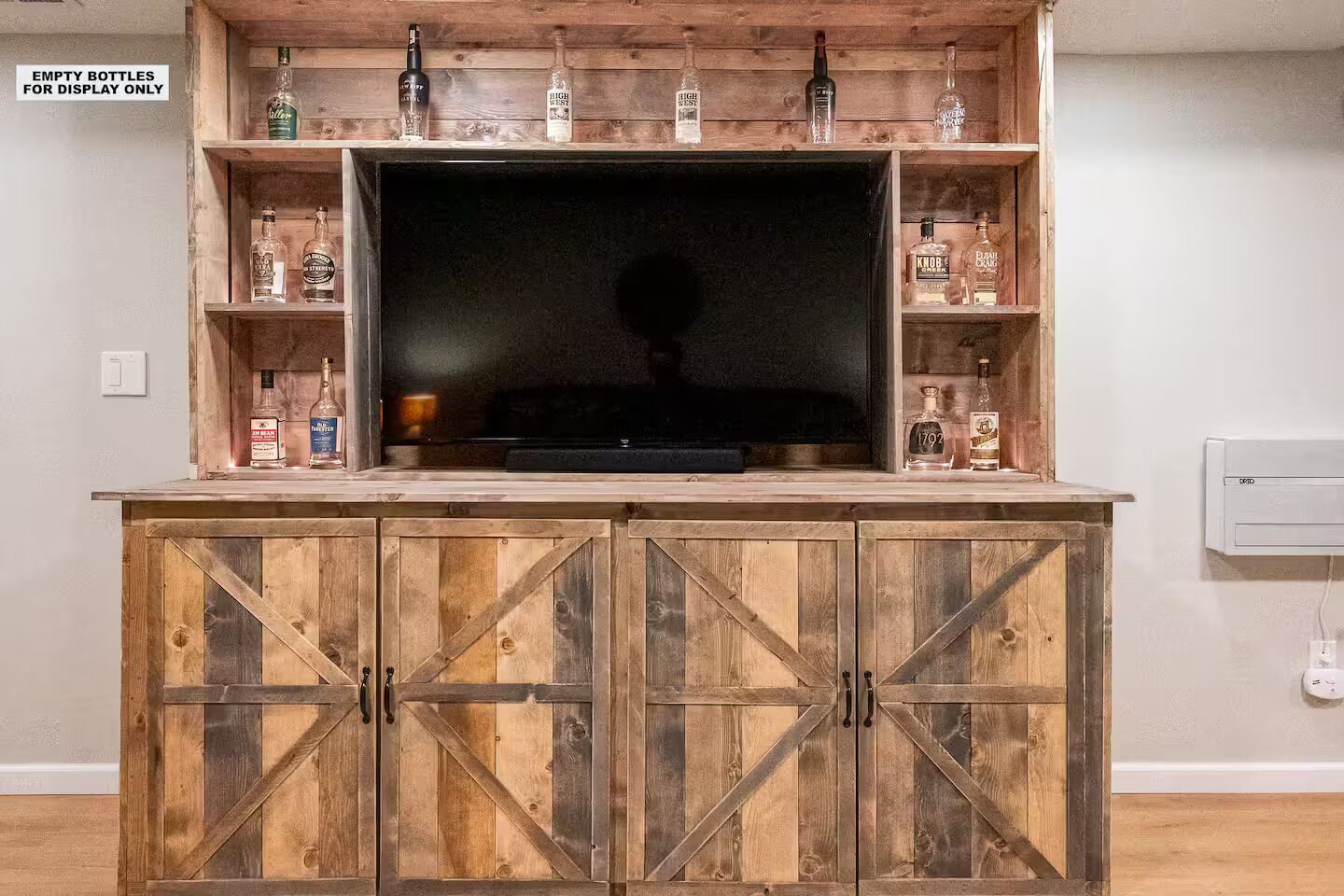 Un mueble de madera para entretenimiento con un televisor y estantes que exhiben varias botellas.