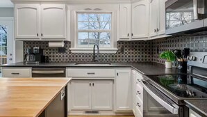 A modern kitchen with white cabinetry, a large window, a built-in stove, and a coffee maker. - Spacious, Pristine Home w/ Firepit, Bourbon Lounge (Bardstown)