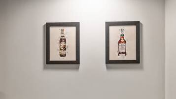 Two framed pictures of a bottle on a white wall, under a single light fixture.