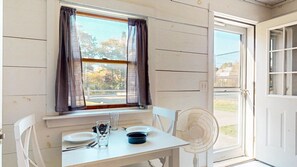 A small dining area with a table, chairs, a fan, and a window with curtains. - Historic Maine Cottage with Wrap-Around Porch & Ocean Views (Boothbay)