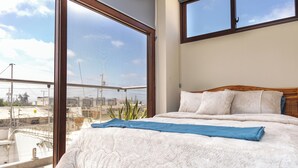 A bedroom with a large window, a bed with a white quilt, and a blue blanket.