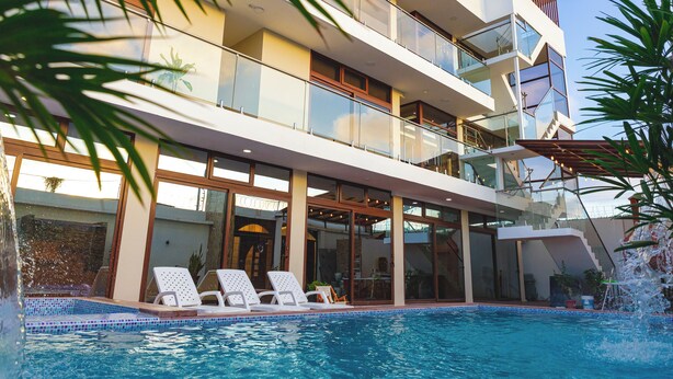 A modern multi-story building with a swimming pool, balconies, and glass railings.
