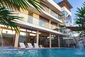 Un immeuble moderne à plusieurs étages, doté d’une piscine, de balcons et de garde-corps en verre.