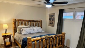 A bedroom with a rustic wooden bed frame, a nightstand with a lamp, and a poster on the wall.