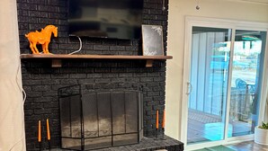 A living room with a black brick fireplace, a flat-screen TV mounted above it, and a ceiling fan.