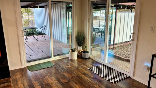 A room with a wooden floor, a sliding glass door leading to an outdoor patio with a table and chairs, and a potted plant.