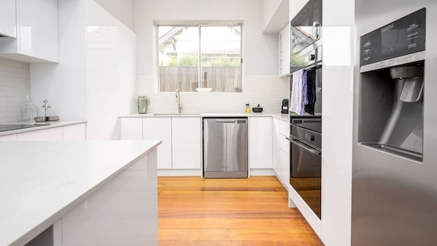 Een moderne keuken met witte kasten, roestvrijstalen apparatuur en een houten vloer.