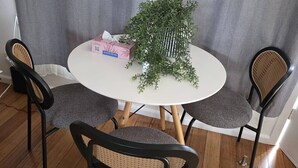 Pyöreä ruokapöytä, jossa on neljä tuolia, ruukkukasvi ja paperinenäliöpakkaus.