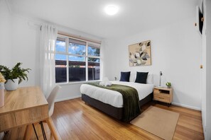 Une chambre à coucher avec un lit, une table de chevet, une lampe et une fenêtre avec des rideaux.