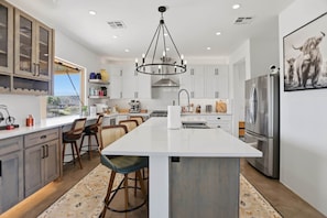A modern kitchen with white cabinetry, a central island with bar stools, stainless steel appliances, and a chandelier.
