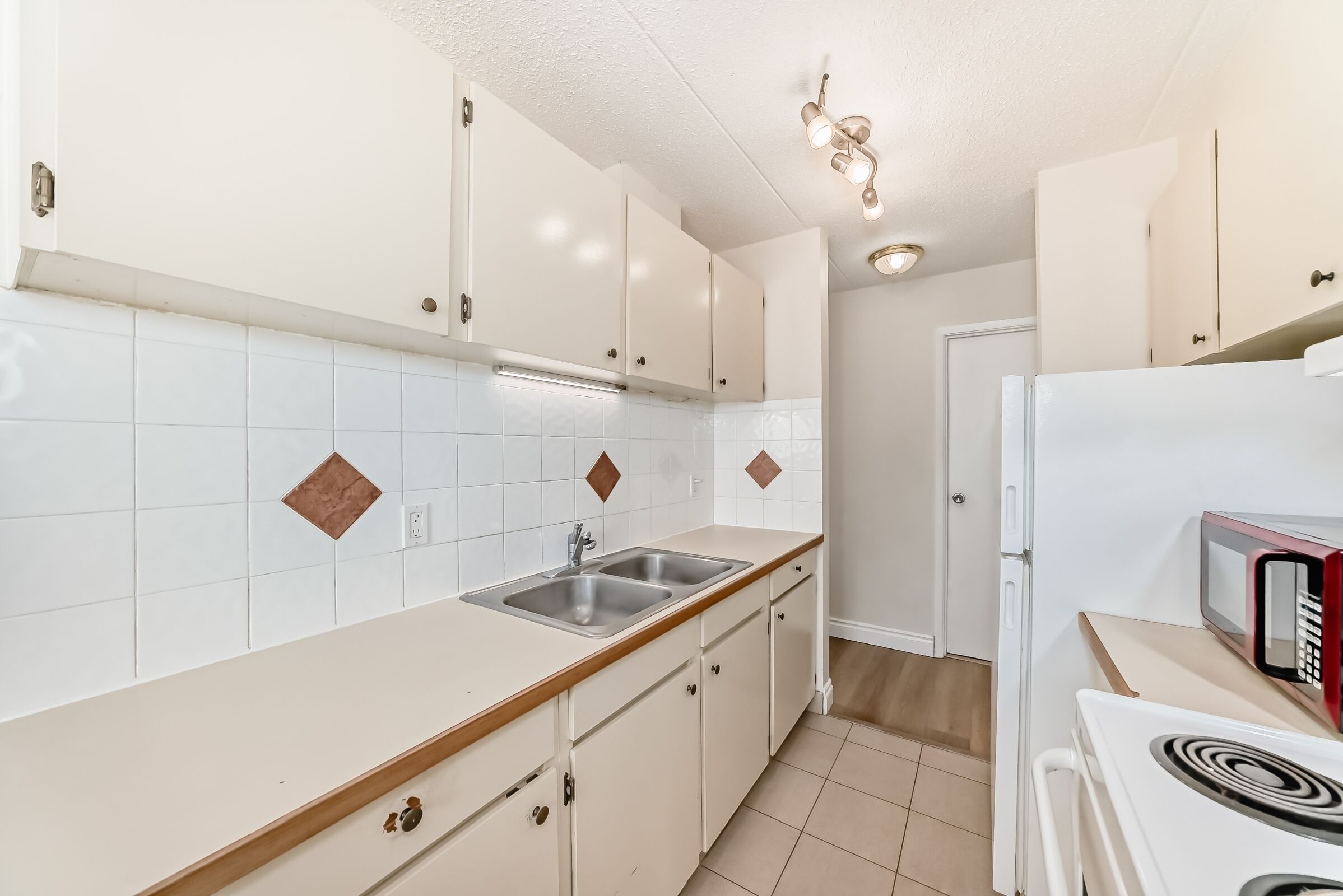 A kitchen with white cabinets, a double sink, a microwave, and a stove.