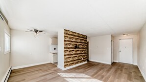 A spacious room with wooden flooring, a ceiling fan, a built-in wooden wall panel, and a door. - Chinook II.
Pet Friendly 
 Nutrien ,CGC Inc Wheatland Plant, De Havilland. (Strathmore)