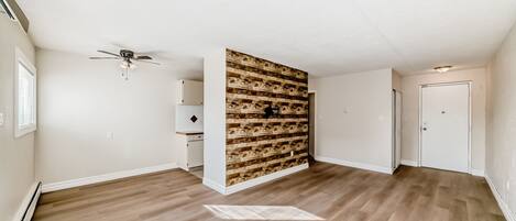 A spacious room with wooden flooring, a ceiling fan, a built-in wooden wall panel, and a door.