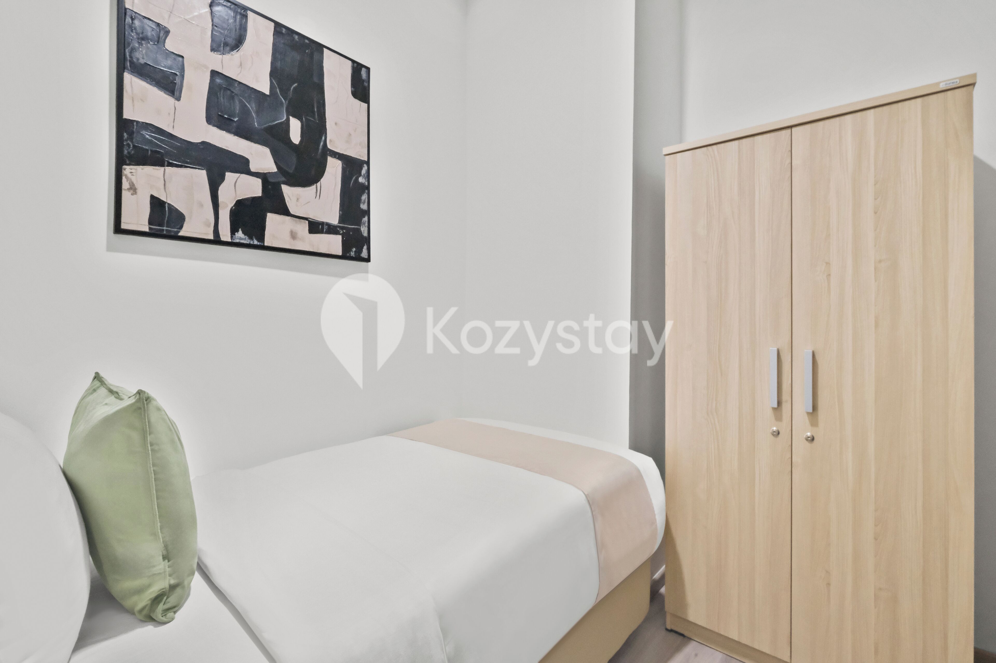 Una habitación con una cama, una almohada verde, un armario de madera y un cuadro abstracto blanco y negro en la pared.