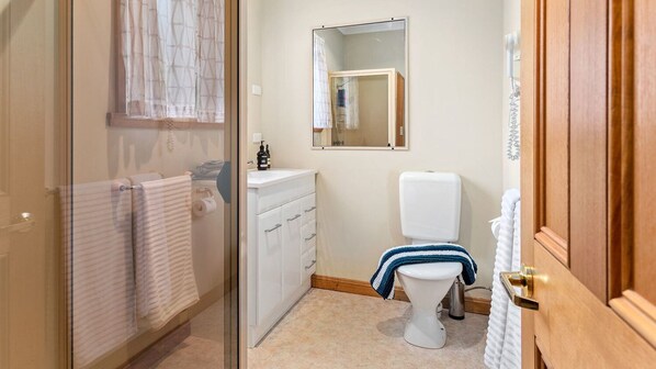 Un baño con inodoro, lavamanos, espejo y toallero.