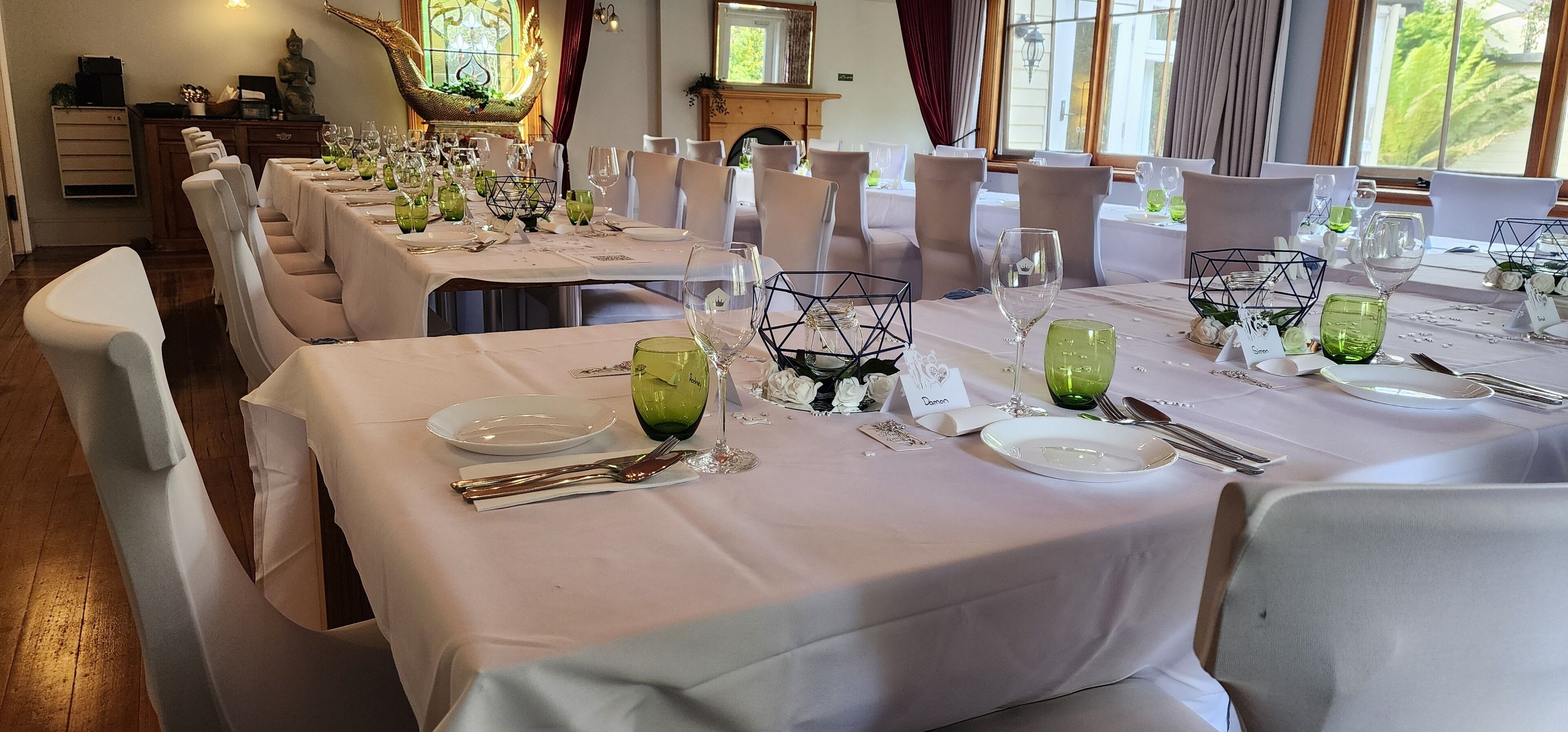 A dining area with multiple tables set for a meal, each with name cards and green glassware.