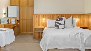 A bedroom with a bed, bedside tables, a wooden wardrobe, a microwave, and a table with a tablecloth.