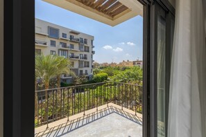 Ein Balkon mit Blick auf ein Wohngebäude, eine Palme und einem Metallgeländer.