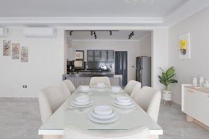 A modern dining area with a glass table set for six, a kitchen in the background, and a potted plant on the side. - Al-Sawah  Upper Duplex 3BR – Eastown Sodic (New Cairo)