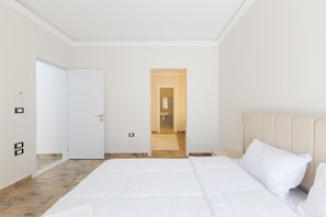 A bedroom with a bed, a door, and a hallway leading to a bathroom. - Al-Sawah  Upper Duplex 3BR – Eastown Sodic (New Cairo)