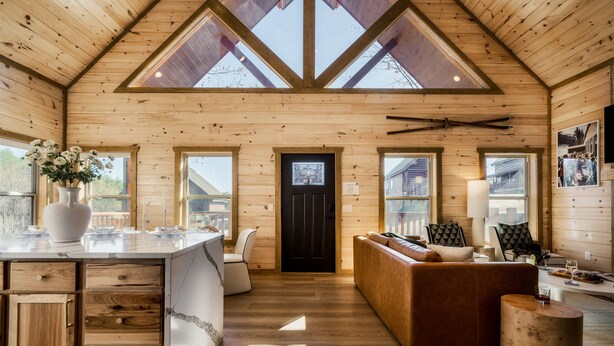 Ein Blockhaus-Innenraum mit einer zentralen Sitzecke, Holzwänden, einem großen Fenster und einem Deckenventilator.
