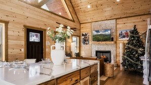 Ein Holzblockhaus-Innenraum mit Kamin aus Stein, einem Weihnachtsbaum und einem großen Fernseher an der Wand.