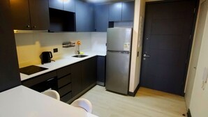 A compact kitchen with dark cabinets, a white countertop, a stainless steel refrigerator, and a small sink. - We have the ideal space for you in Ñuñoa (Ñuñoa)