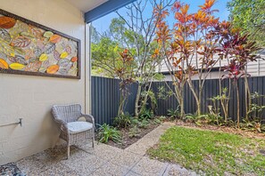 A patio area with a wicker chair, a mosaic wall, and a variety of plants.