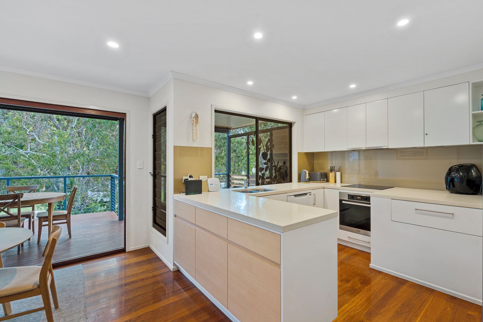 Una cocina moderna con armarios blancos, una isla central y un comedor con mobiliario de madera.