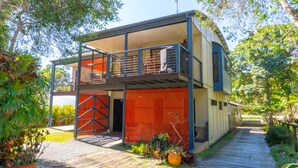 A two-story building with a balcony on the upper floor, a red gate, and a paved pathway leading to the entrance. - Melaleuca Lookout - Modern 3-Bedroom Townhouse with Ocean Wiews (Point Lookout)