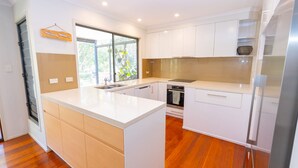 A modern kitchen with white cabinetry, a large island, and a built-in oven. - Melaleuca Lookout - Modern 3-Bedroom Townhouse with Ocean Wiews (Point Lookout)