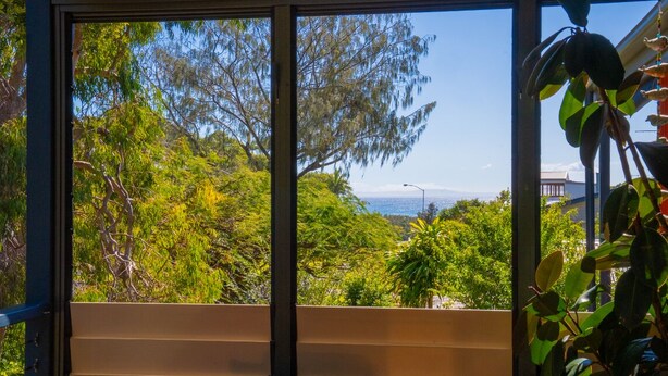 A room with a large window offering a view of lush greenery and a distant body of water. - Melaleuca Lookout - Modern 3-Bedroom Townhouse with Ocean Wiews (Point Lookout)