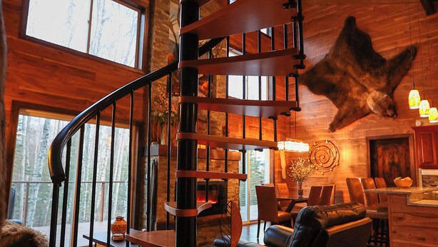 Una escalera de caracol en un interior de madera con un animal disecado colgado, ventanas amplias y un comedor.