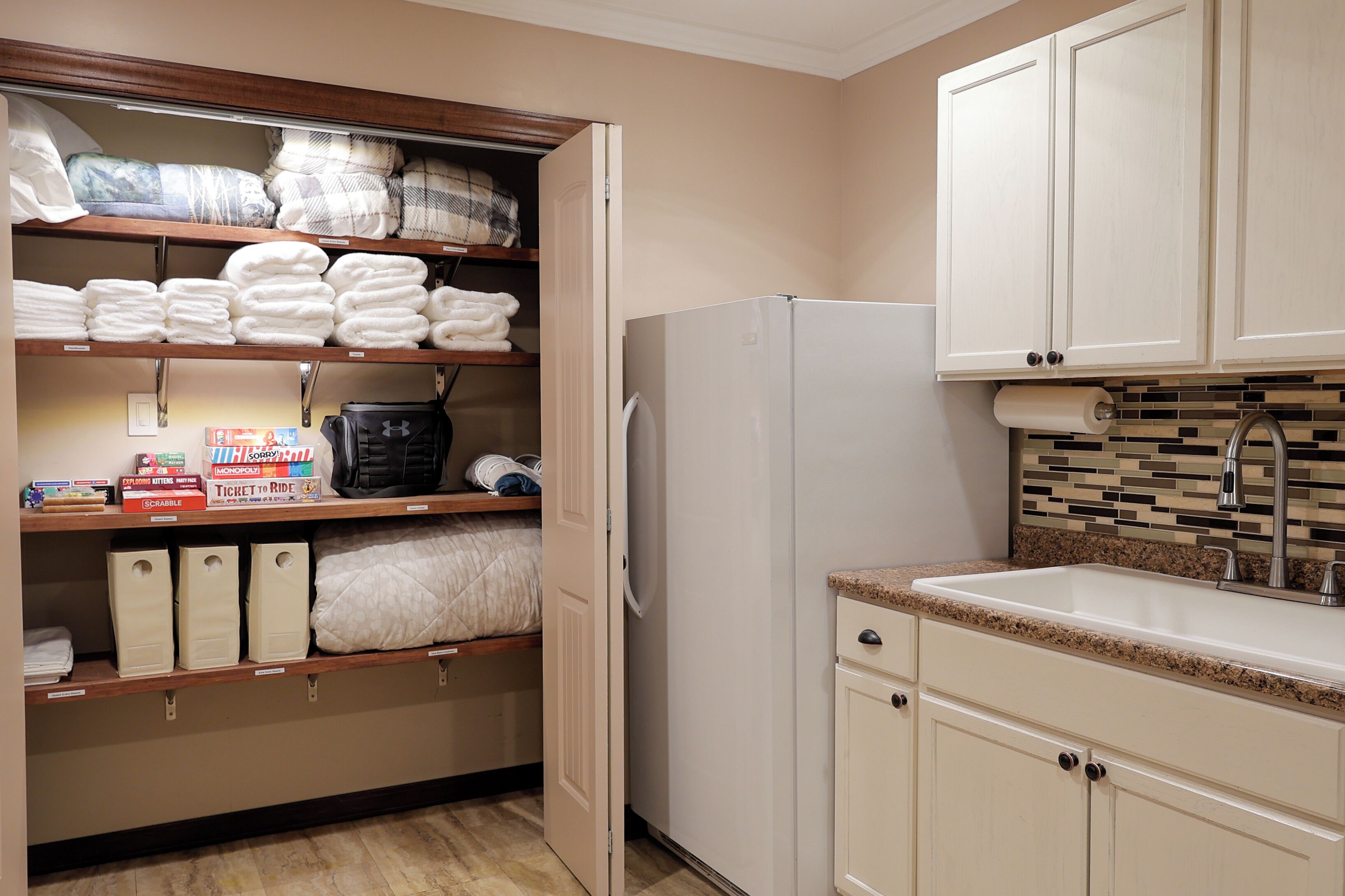 A kitchen with a refrigerator, a sink, and shelves with towels and toiletries.