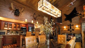 Una cocina moderna con armarios de madera, un comedor con mesa de vidrio y sillas de cuero, y una chimenea con trofeos de animales.