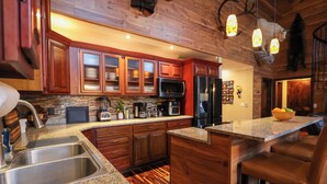 Una cocina con armarios de madera, encimeras de granito, electrodomésticos de acero inoxidable y una zona de bar con asientos de cuero.